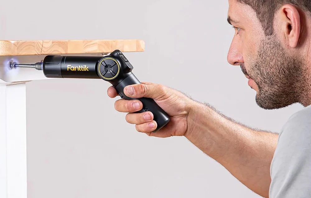 A man fastens a screw in a countertop using an electric screwdriver with an adjustable handle.