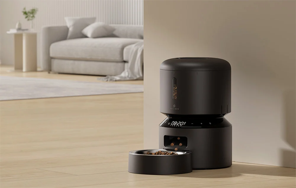 The automatic feeder stands on the living room floor and dispenses food into the bowl