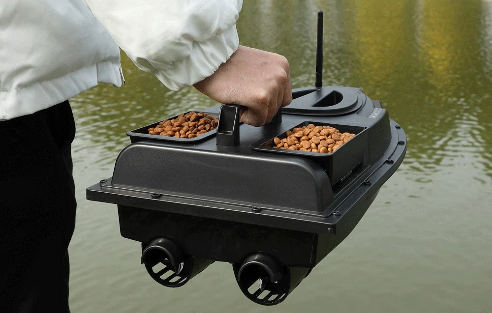 Angler in a white jacket holding a black RC bait boat with two pellet containers above the water