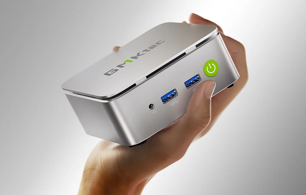 A silver Mini PC held in hand with various ports.