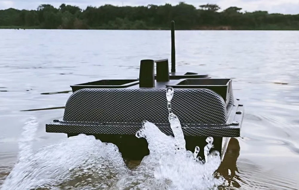 Carbon bait boat from the back with water fountain on the lake, empty containers and antenna on top visible