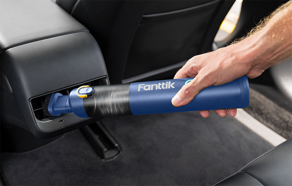 A hand cleans a car vent using the Fanttik cordless portable car vacuum cleaner.