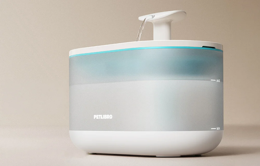An automatic pet water fountain with a translucent reservoir and a stream of water flowing from the top nozzle.