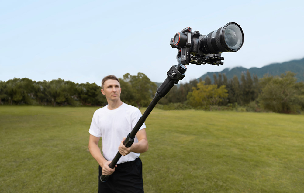 Boy holding an extended gimbal with attached camera outdoors