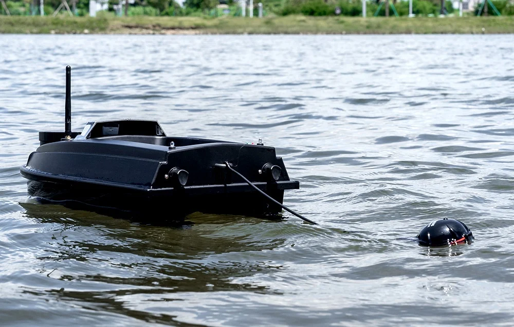A black bait boat with an antenna and a sonar sensor on a line, floating on a lake