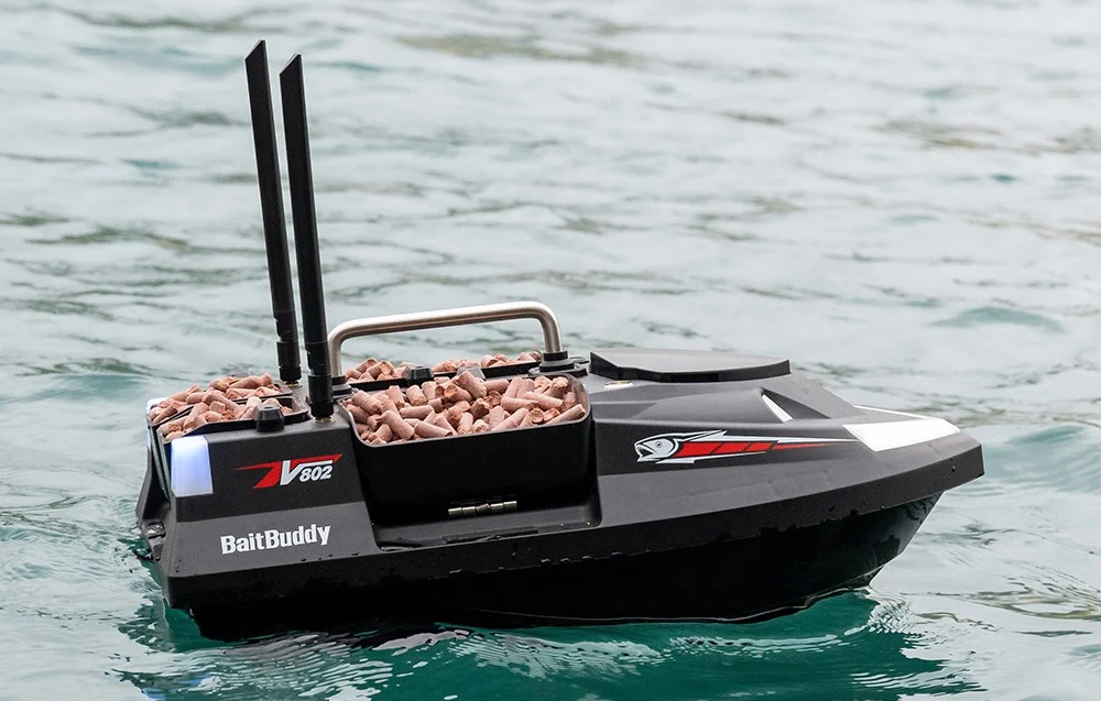 BaitBuddy V602 RC bait boat with pink pellets floating on clear turquoise water