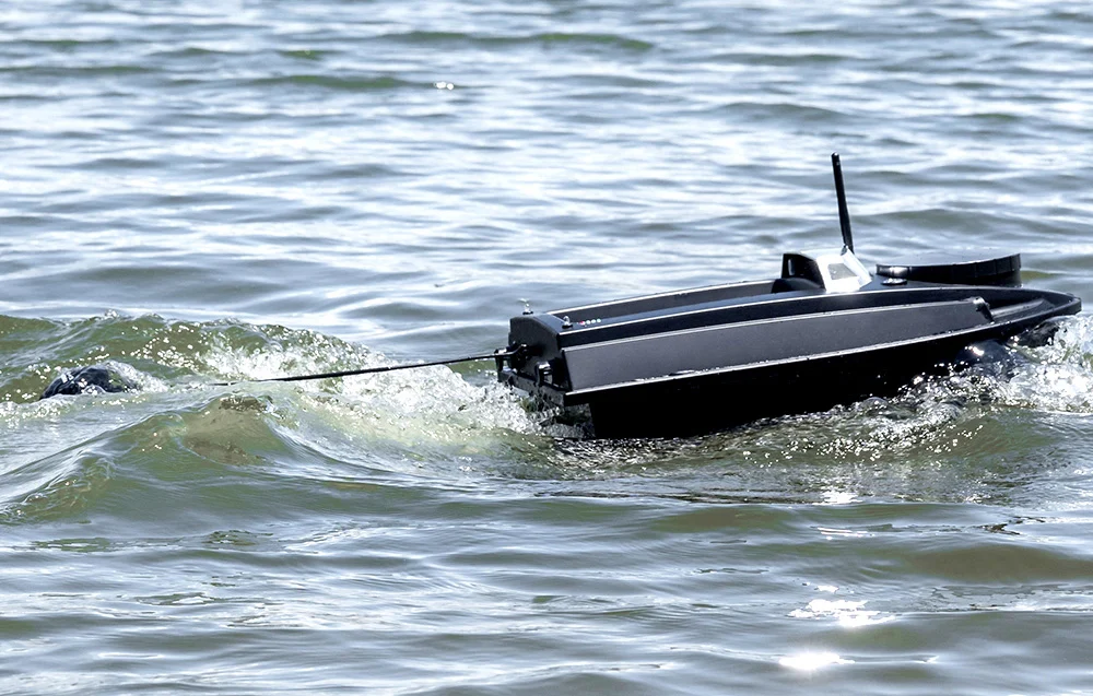 A black bait boat with an antenna floating on the calm waters of a lake