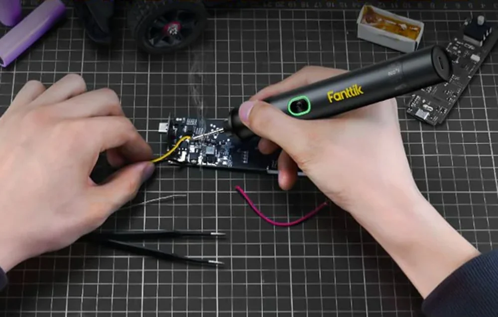 A person soldering a wire to a circuit board using a black Fanttik soldering iron.
