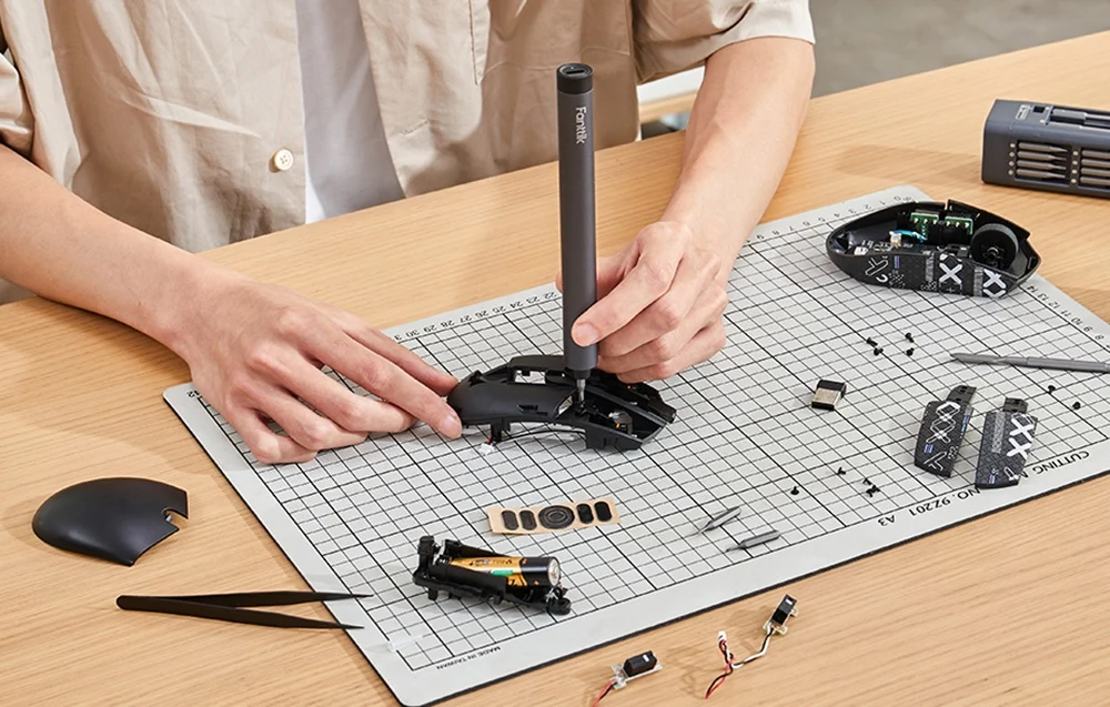 A man sits at his desk and repairs a computer mouse with a precision screwdriver.