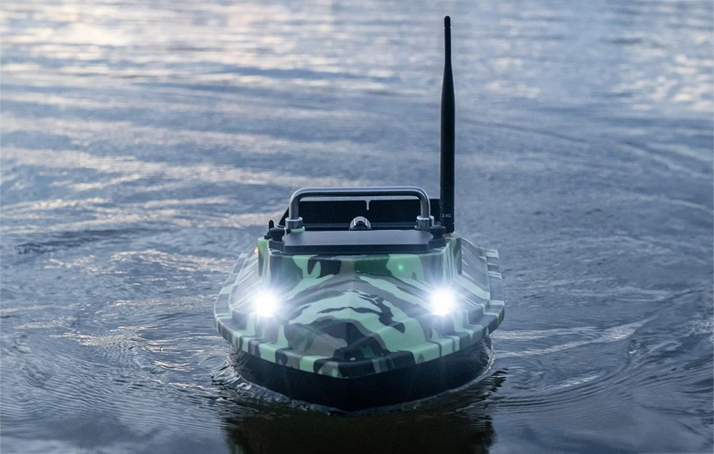 A bait boat in moro camouflage with LED headlights on floating on the water in the evening