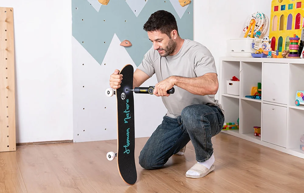 A man repairs a skateboard in a child's room with an electric screwdriver.