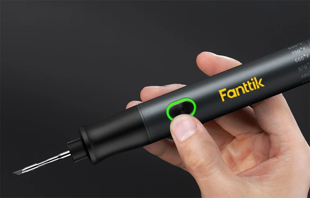 Close-up of a hand holding the Fanttik black soldering iron with the green button light on.