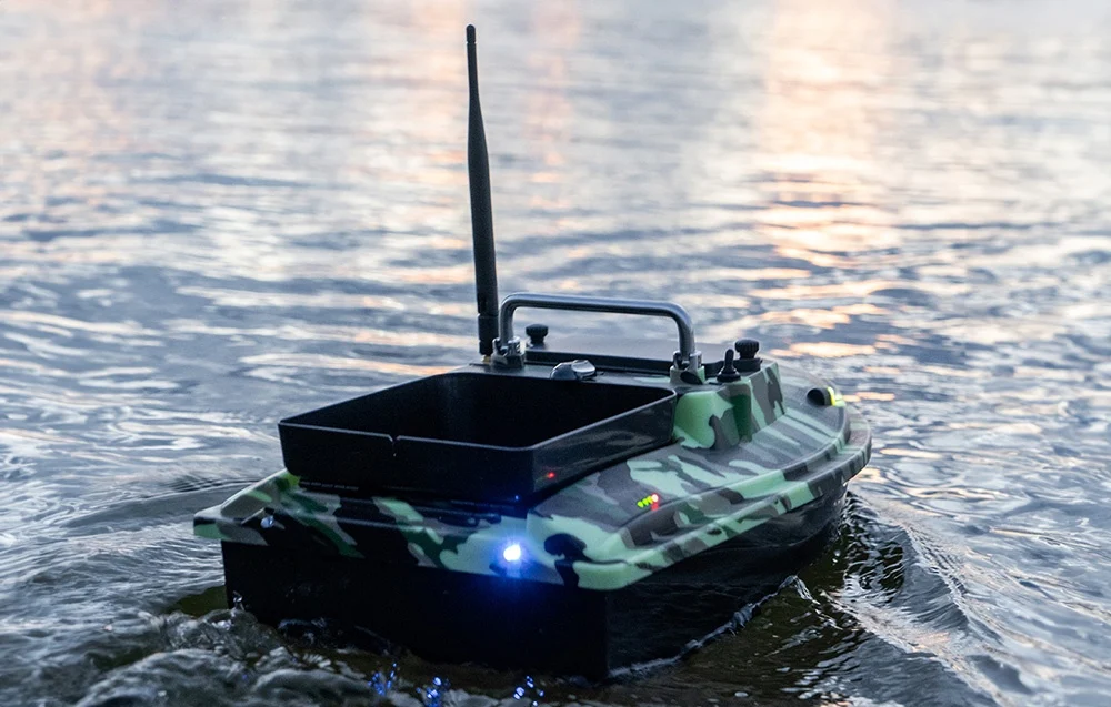 RC bait boat in moro camouflage with blue lighting floating on the lake at dusk
