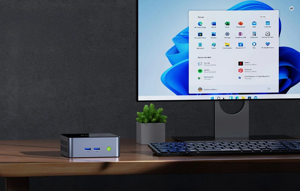 A silver GMKtec mini PC on a desk next to a monitor running Windows 11.