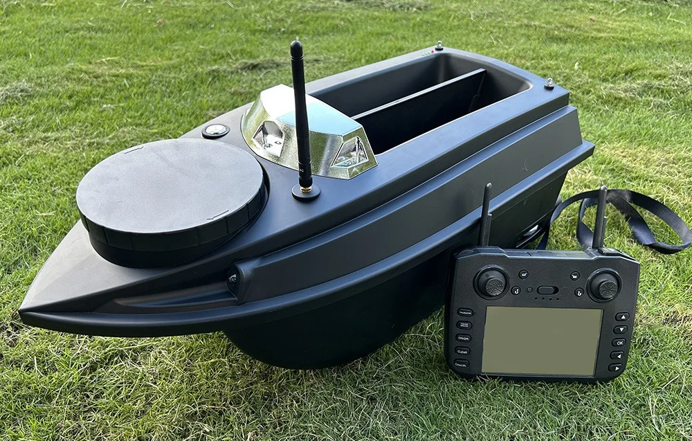 Black bait boat with two compartments and a remote control with a display on the grass