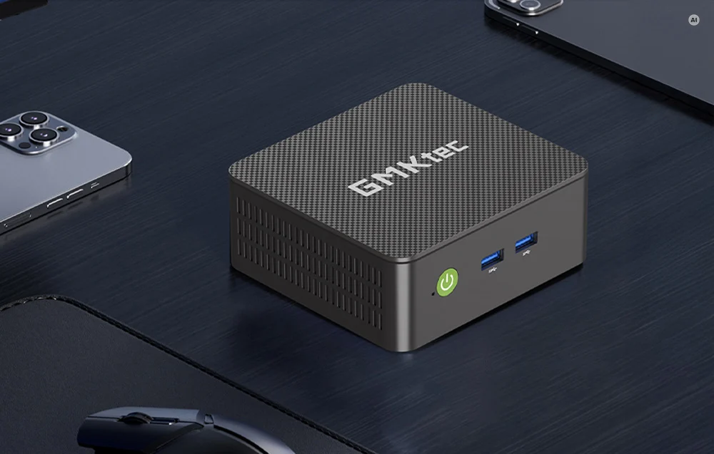 The GMKtec Mini PC with a carbon-fiber-textured top surface, sitting on a desk next to a smartphone and a mouse.