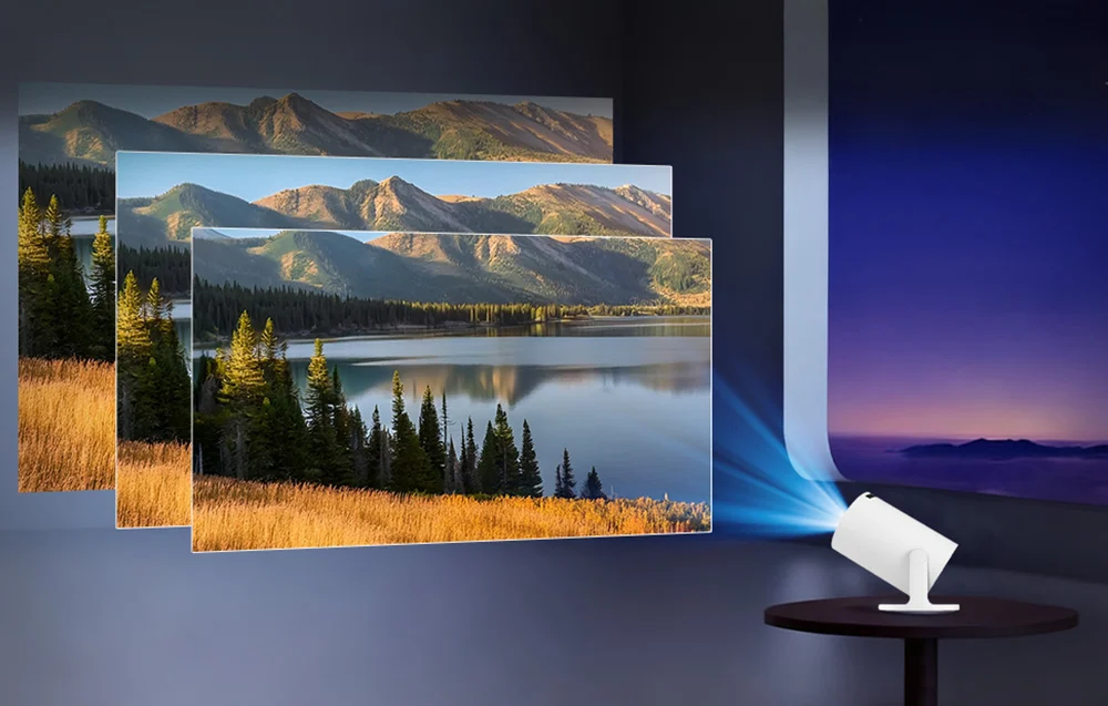 The projector, placed on a table, displays three overlapping images of a mountain landscape with a lake on the wall, demonstrating projection scaling
