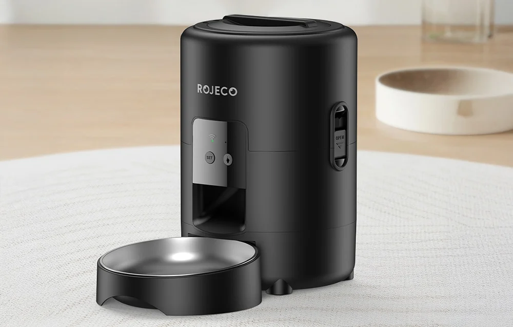 Black automatic food dispenser on a white carpet in a bright room
