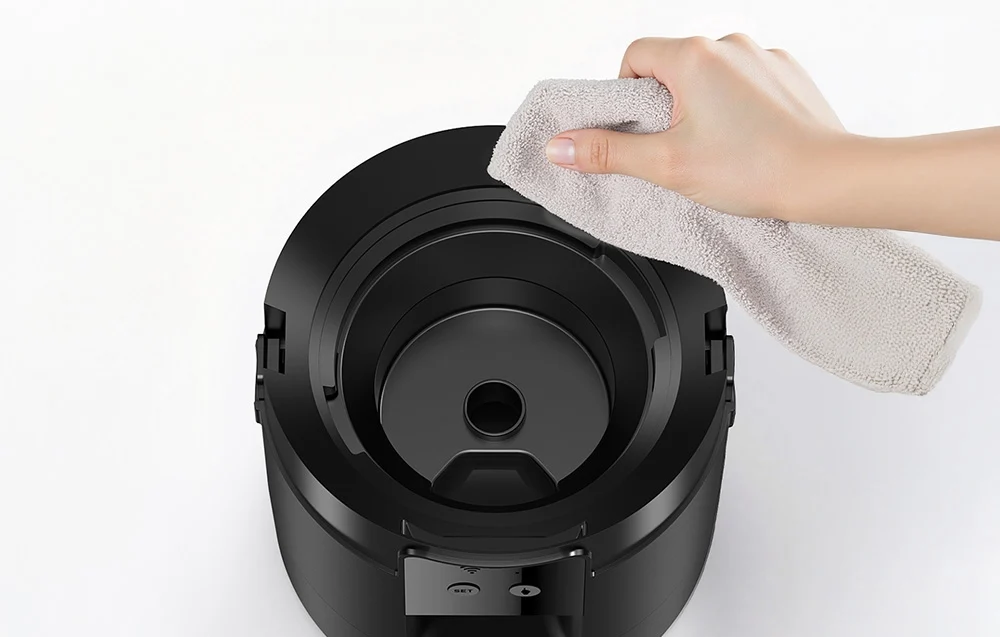 Hand cleaning black food dispenser with gray cloth on light background